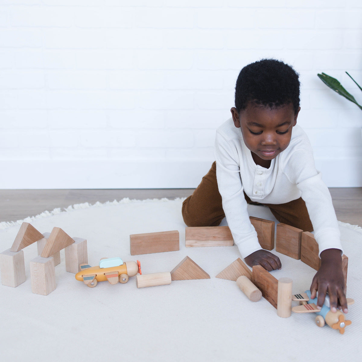 SpiritnSprout: Child playing with wooden airplanes and blocks on the floor