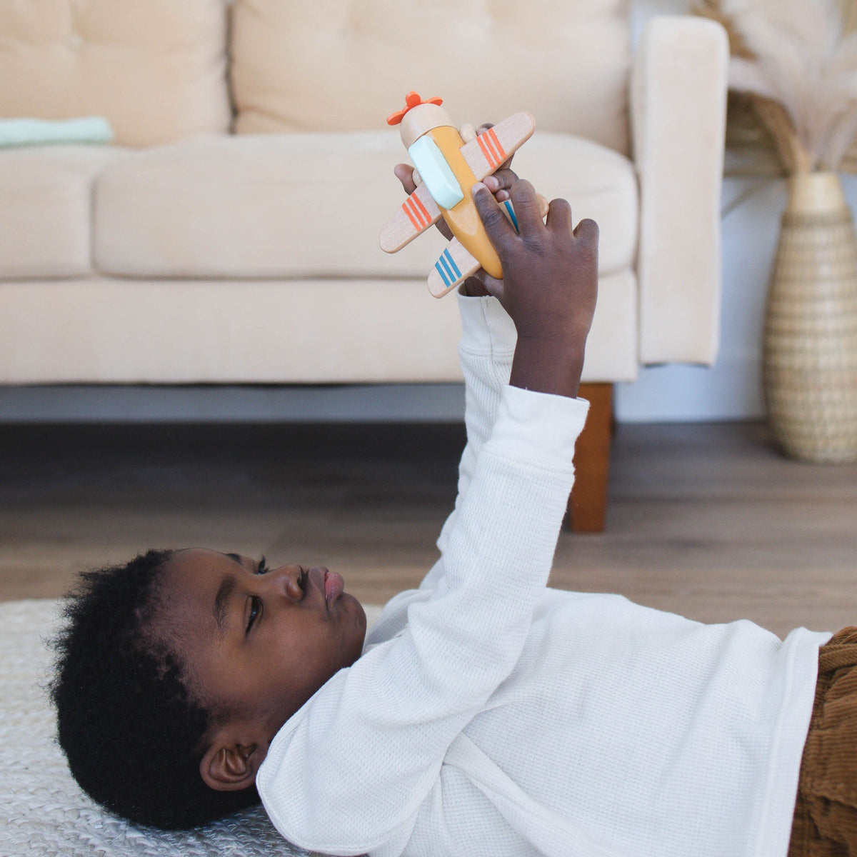 SpiritnSprout: Child lying on a rug and holding a toy airplane overhead