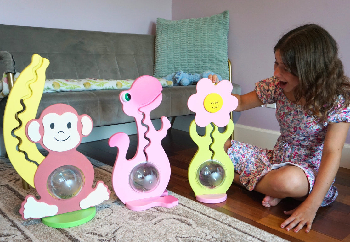 Child sitting beside monkey, pink dinosaur and flower coin banks