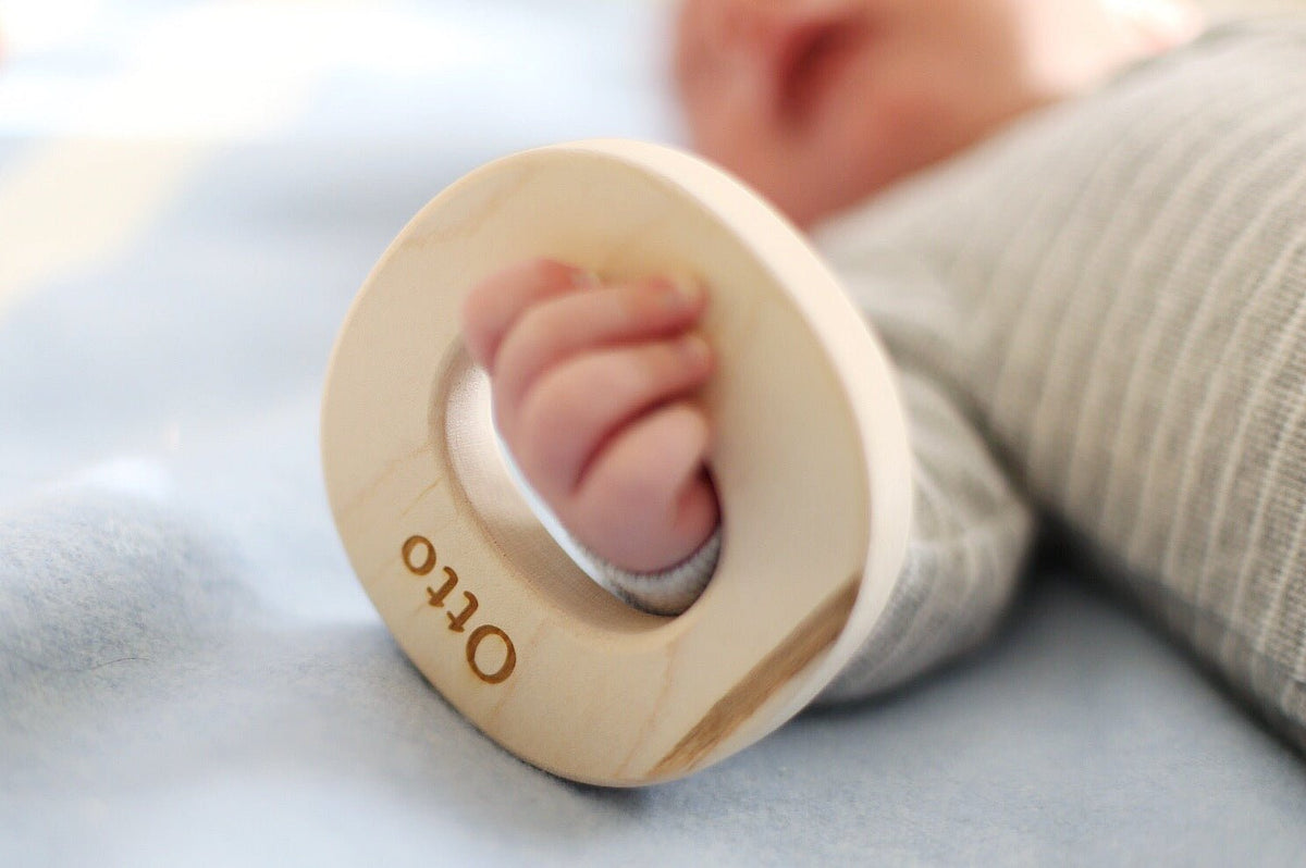 Close-up of a baby holding an O-shaped wooden grasping toy with example engraving