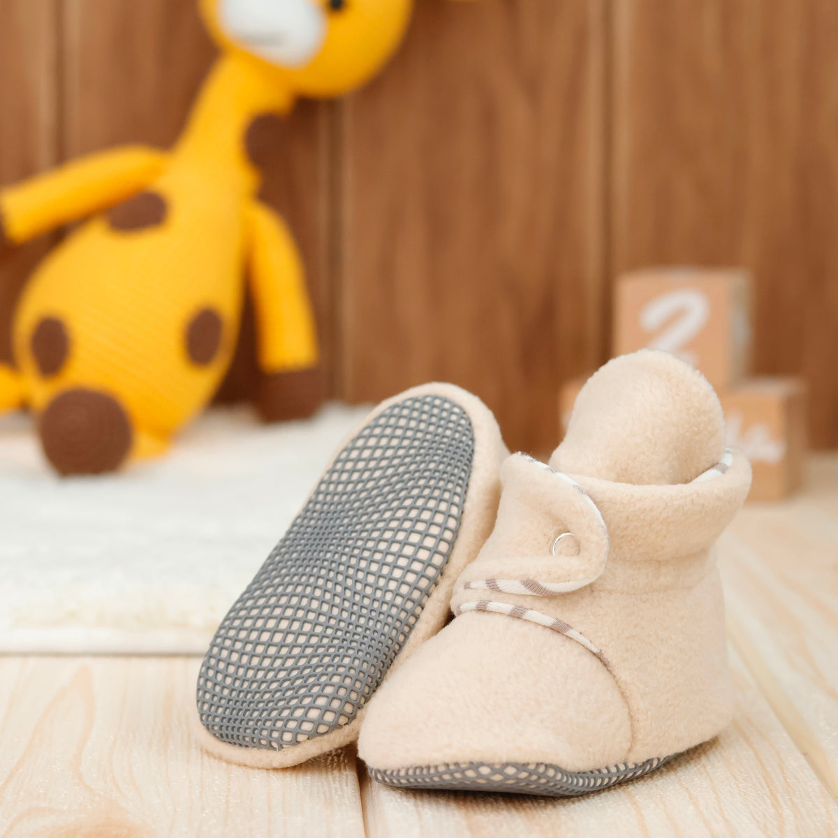 Cream fleece baby booties with pale striped lining and snap straps arranged on a surface with one sole facing the camera.