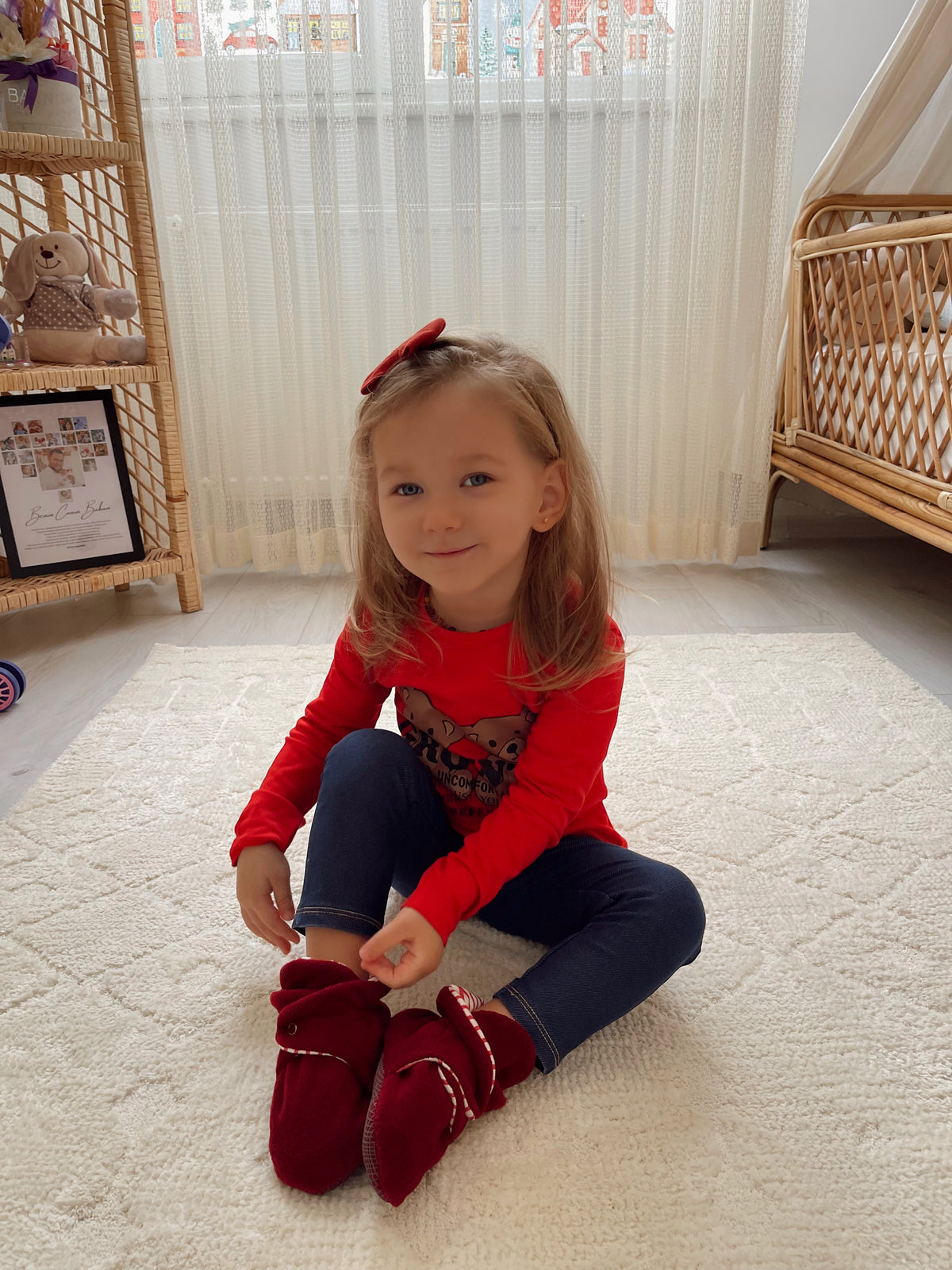 Child seated on a stair wearing a red sweater and burgundy booties.
