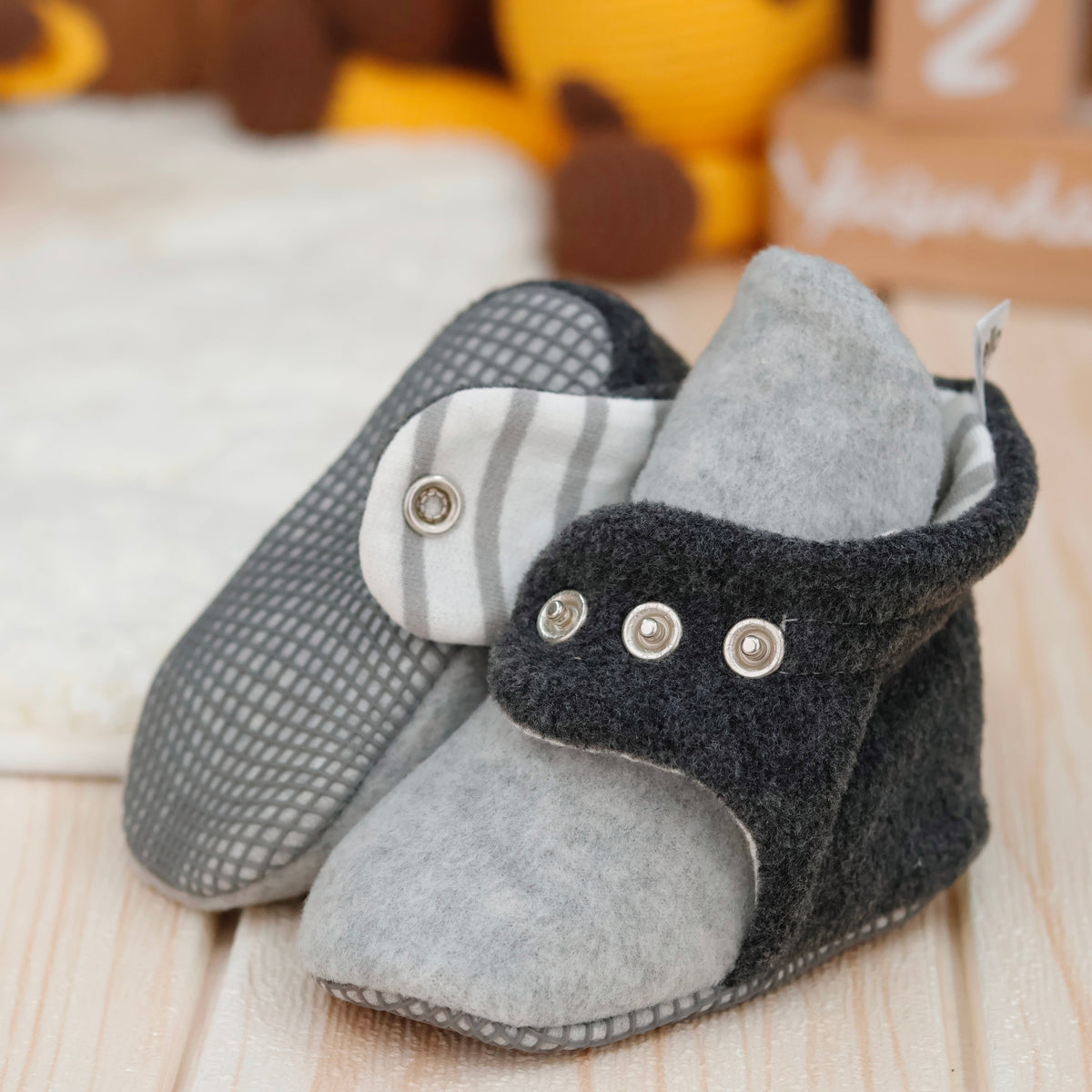 Close-up of gray-and-charcoal fleece baby booties with striped lining and snap straps, showing one sole and an open snap strap.