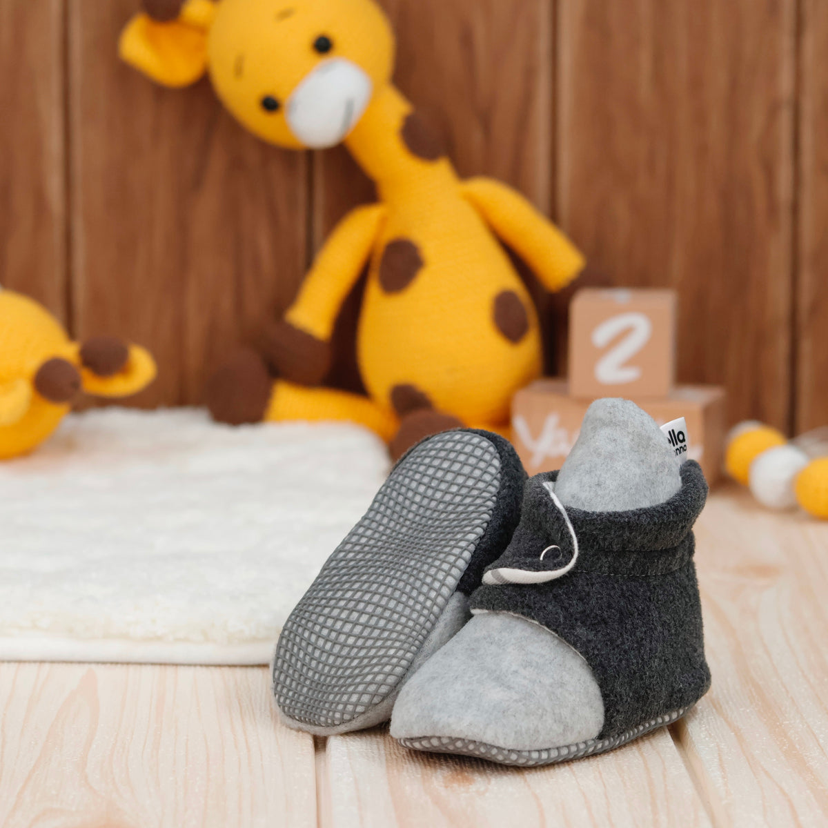 Gray-and-charcoal fleece baby booties with striped lining and snap straps arranged on a surface with one sole facing the camera.