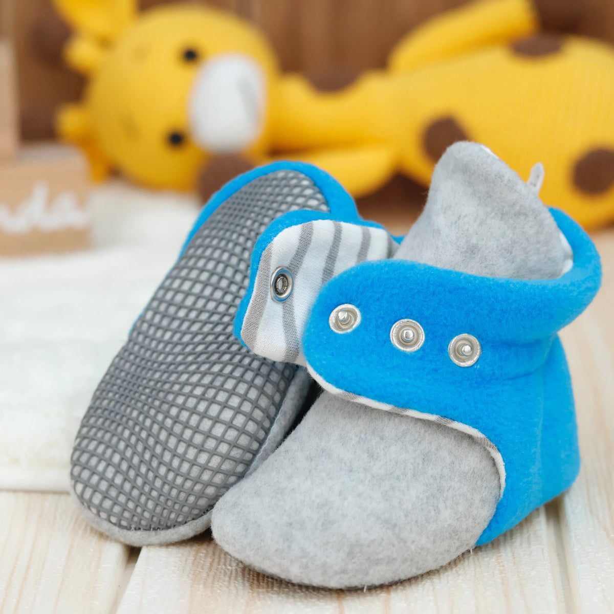 Close-up of blue-and-gray fleece baby booties with striped lining and snap straps, showing one sole and an open snap strap.