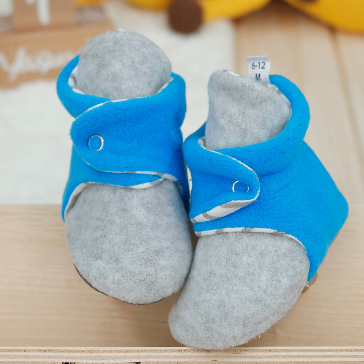 Front view of a pair of blue-and-gray fleece baby booties with striped lining and snap straps.
