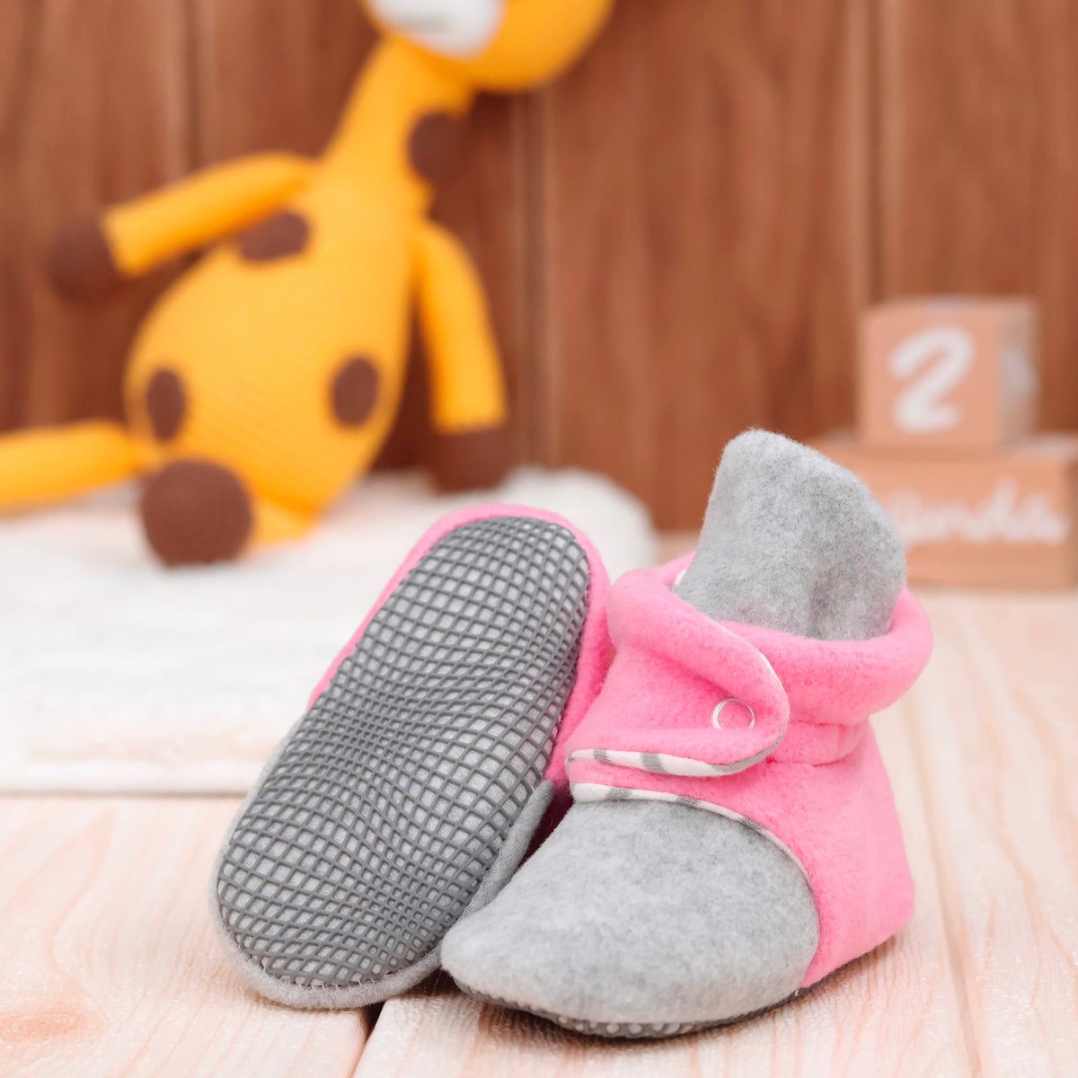 Pink-and-gray fleece baby booties with striped lining and snap straps arranged on a surface with one sole facing the camera.