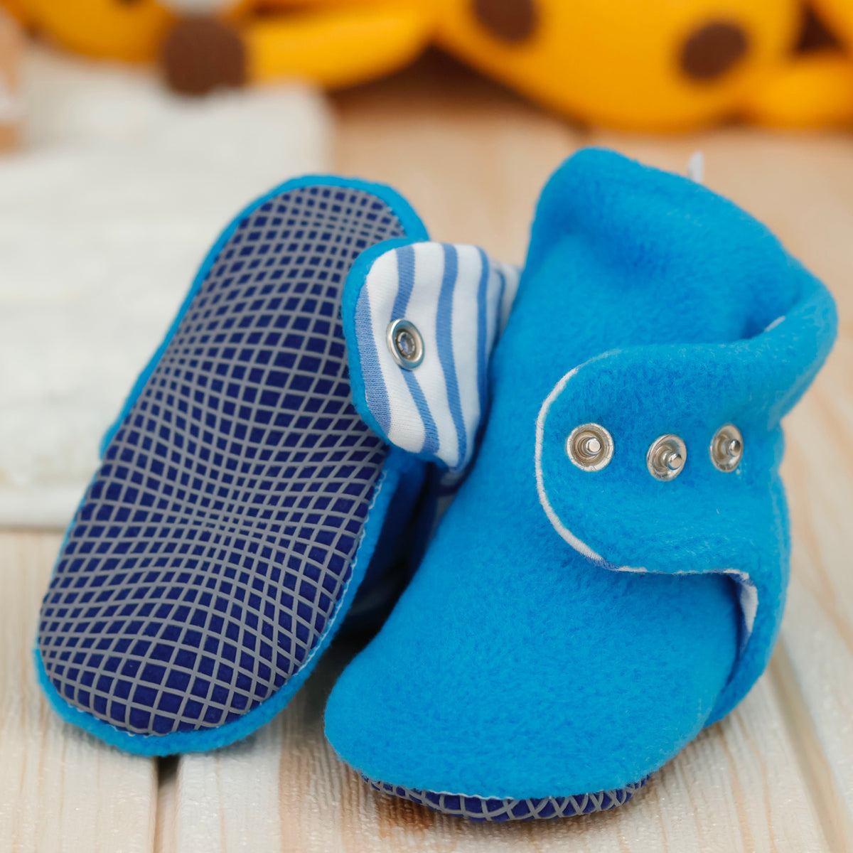 Close-up of bright blue fleece baby booties with striped lining and snap straps, showing one sole and an open snap strap.