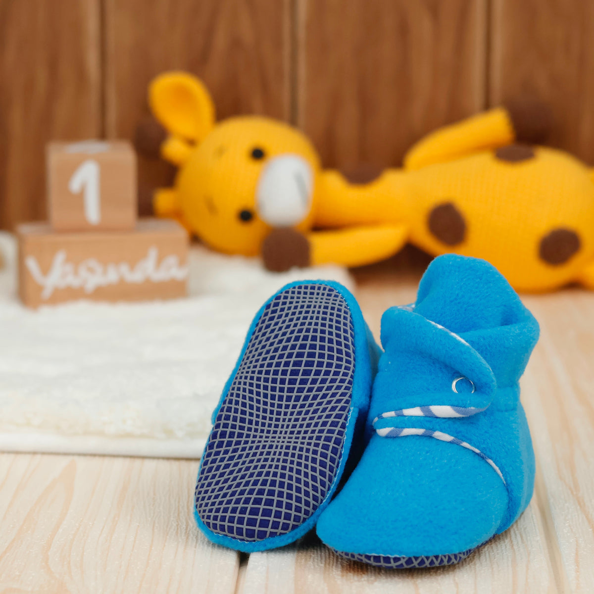 Bright blue fleece baby booties with striped lining and snap straps arranged on a surface with one sole facing the camera.