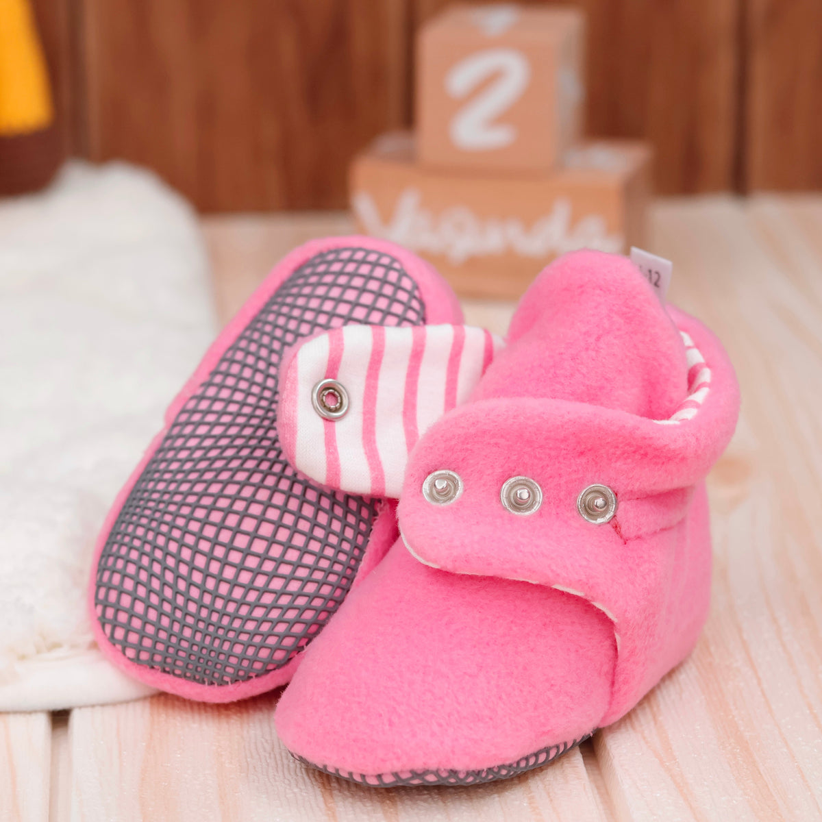 Close-up of pink fleece baby booties with striped lining and snap straps, showing one sole and an open snap strap.