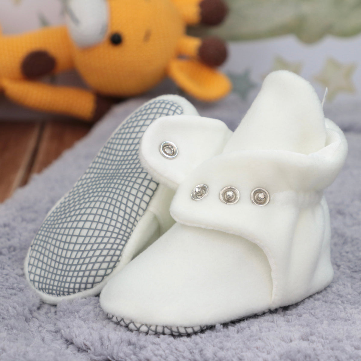 Close-up of white fleece baby booties with snap straps, showing one sole and an open snap strap.