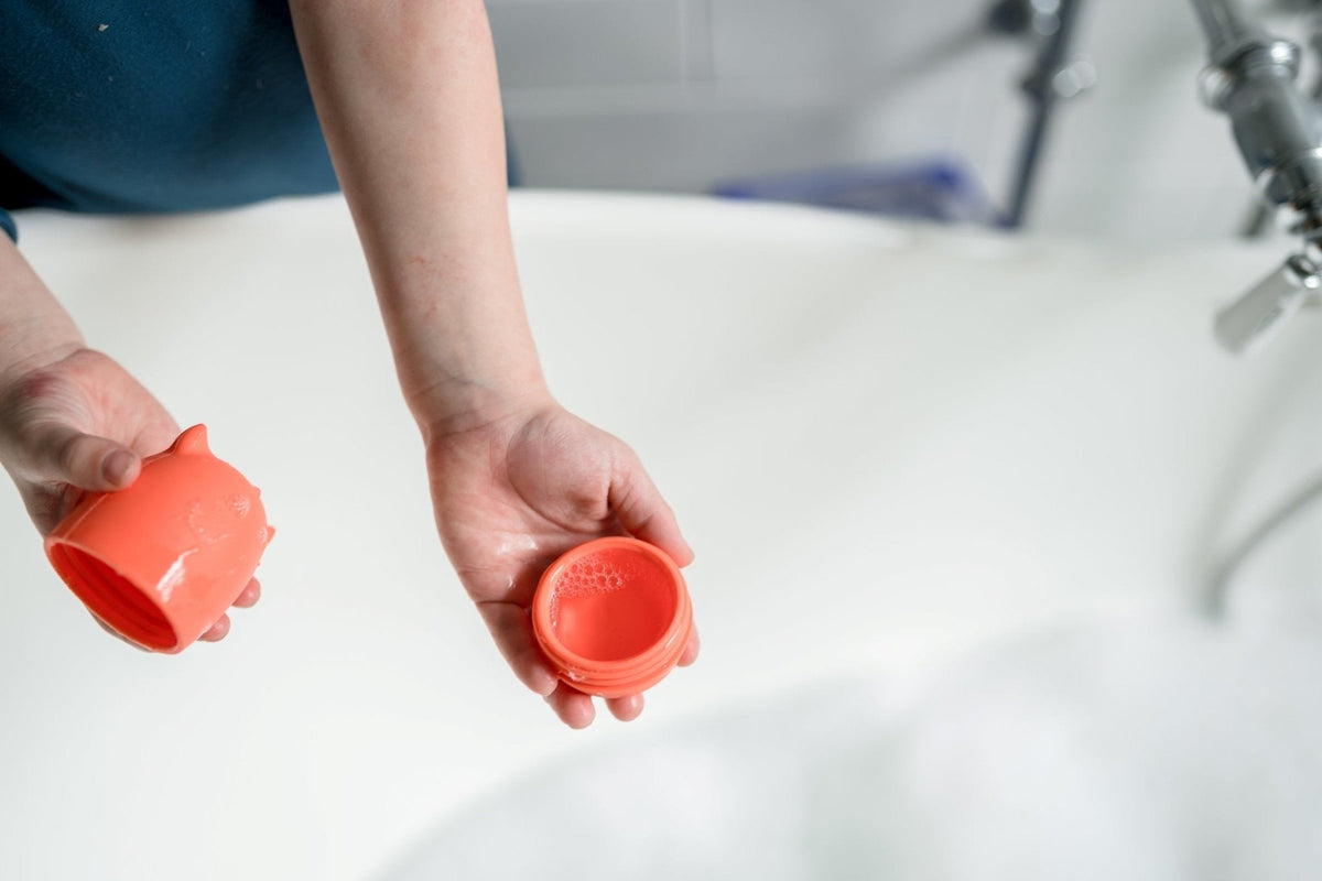 Hands separating the two halves of a red silicone Bath Buddy over a bathtub