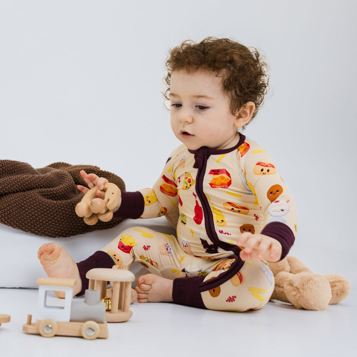 Baby seated beside a toy vehicle while wearing Bam & Stitch Blissful Bites Convertible Romper.