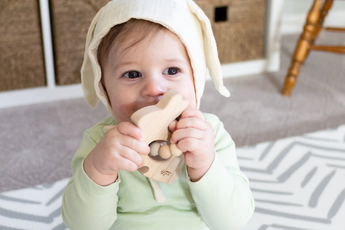 Baby holding a bunny-shaped wooden grasping toy without visible silicone beads
