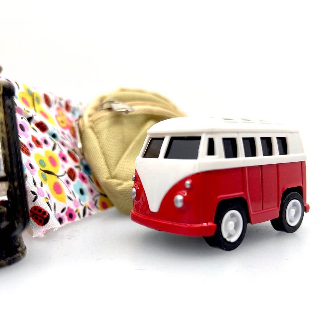 Red-and-white toy camper van beside a miniature backpack and patterned tent