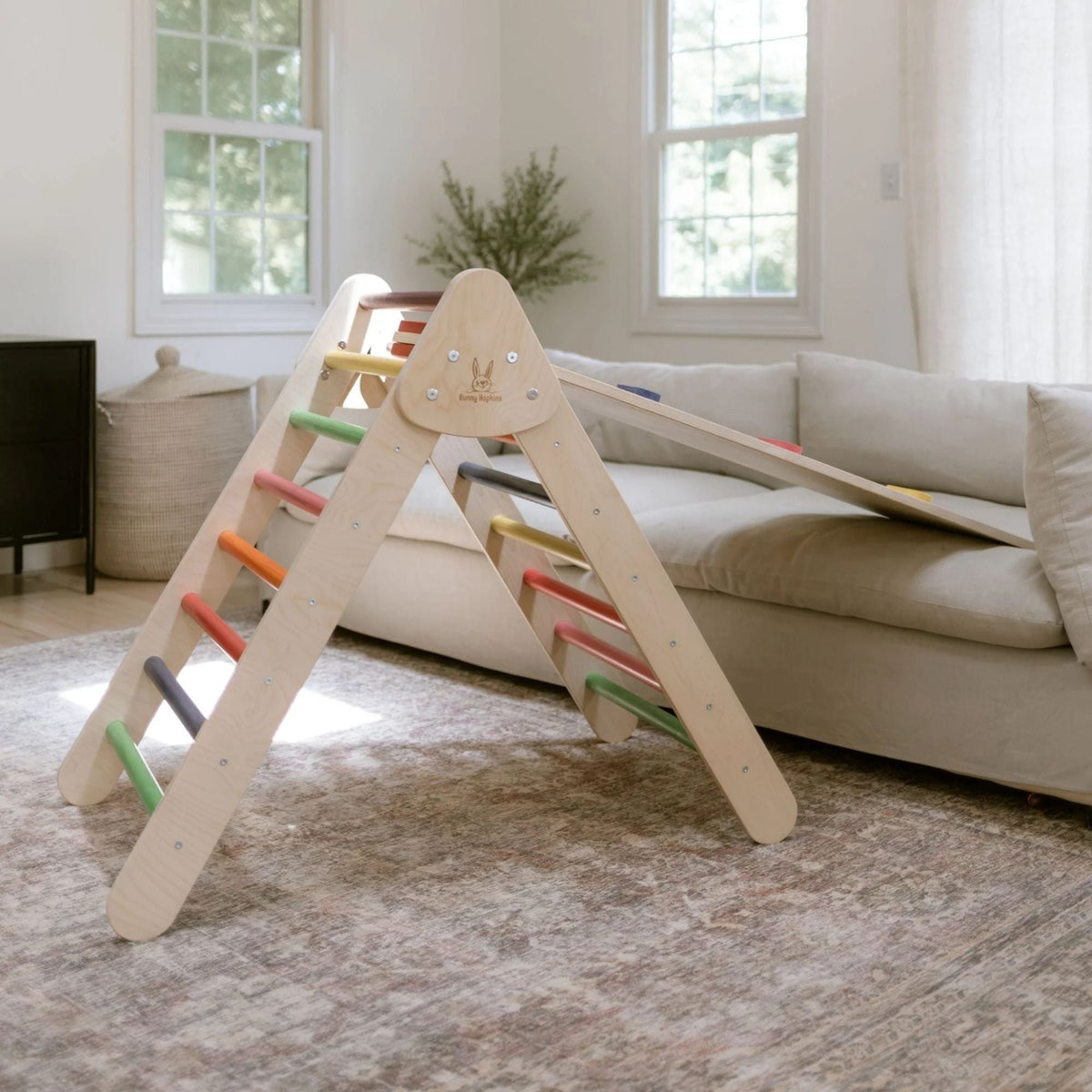 Rainbow-rung climbing triangle with a smooth ramp resting on a sofa.