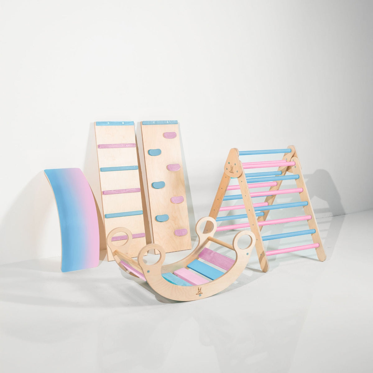 Pastel blue and pink climbing triangle, two ramps, curved wobble board and rocker displayed together.