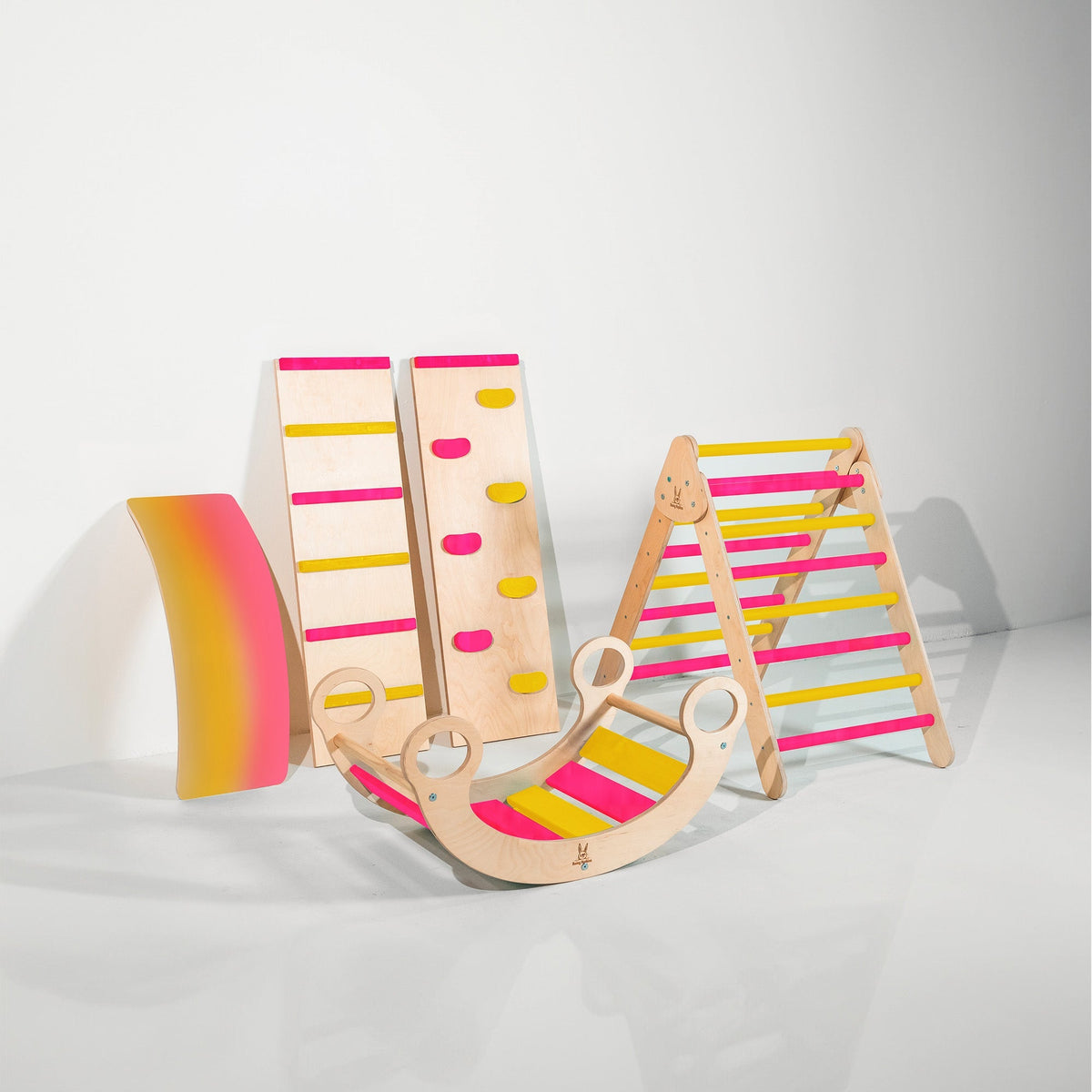 Pink and yellow climbing triangle, two ramps, curved wobble board and rocker displayed together.