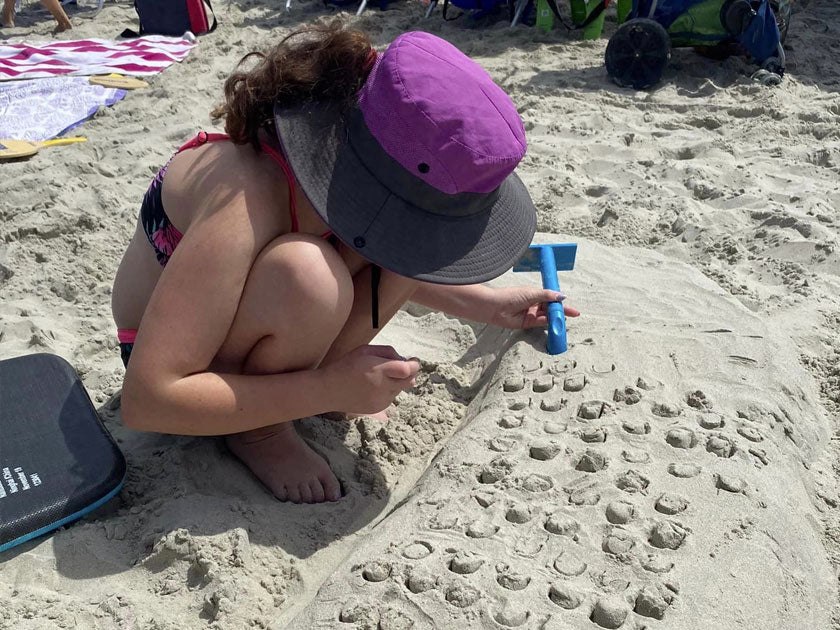 Person using a blue tool to add a repeating scale pattern to a long sand sculpture.