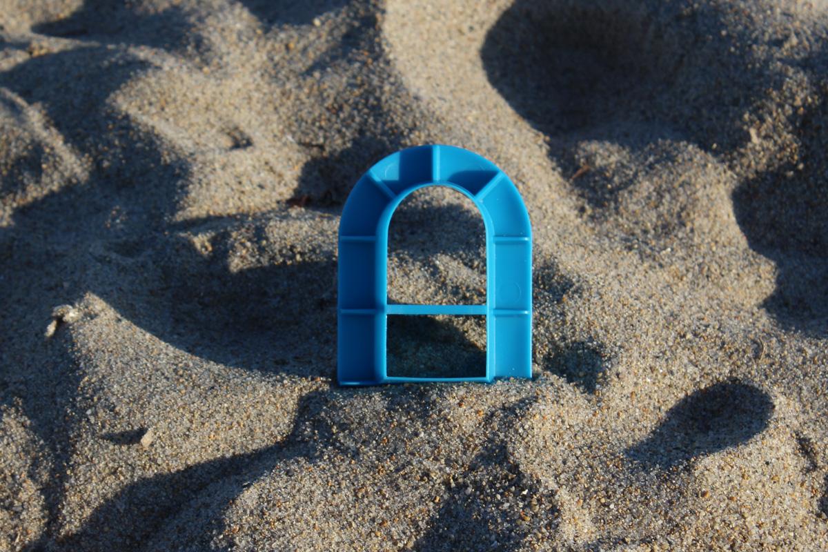 Blue arched window cutter viewed from its divided back side, standing upright in beach sand.