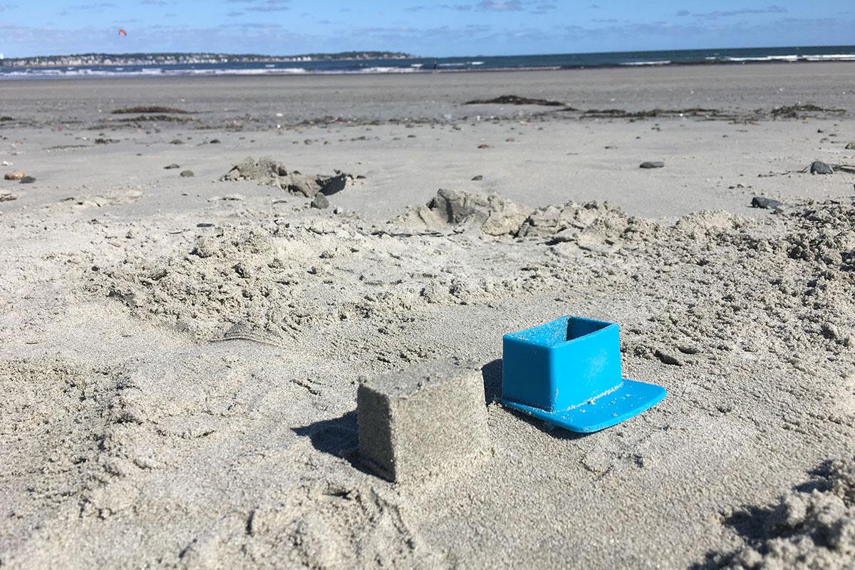 Blue rectangular battlement form beside a freshly molded sand block on the beach.