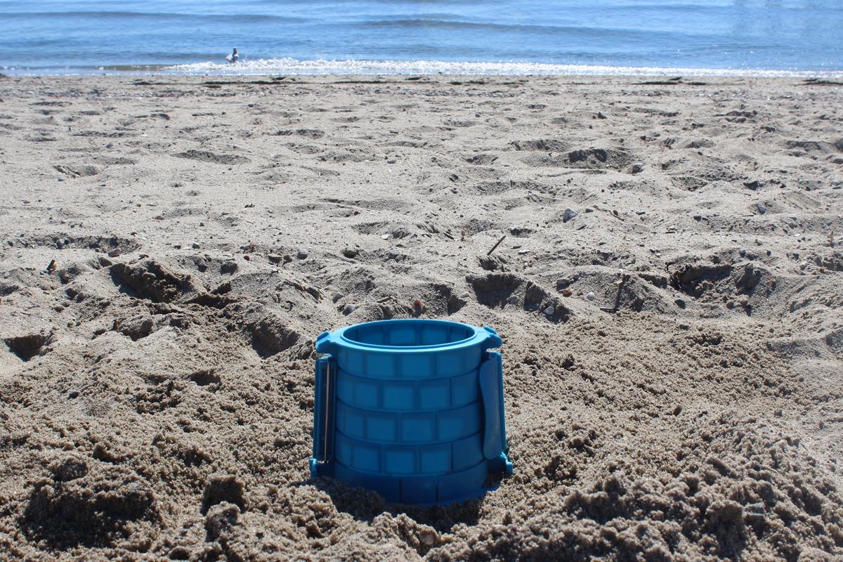 Small blue brick-pattern tower mold standing on the beach with the sea behind it.