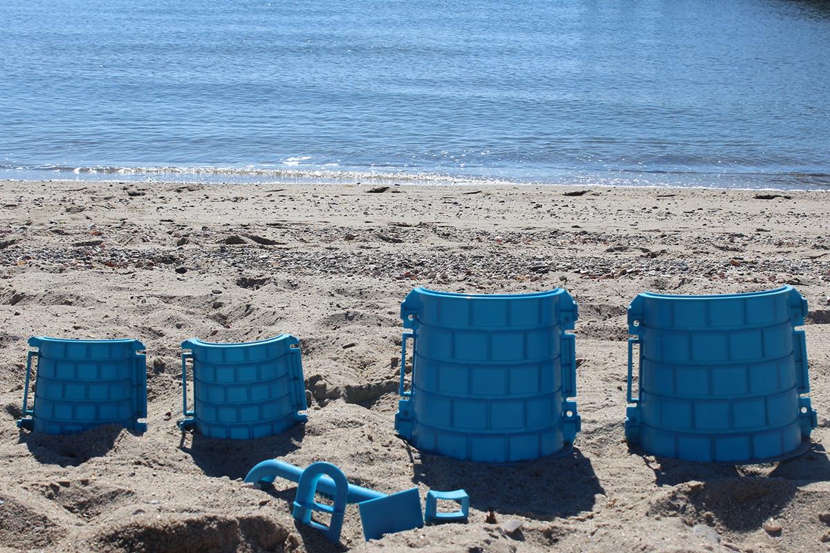 Two blue split tower molds opened into four halves, with window cutter, battlement form and sculpting tool on the beach.