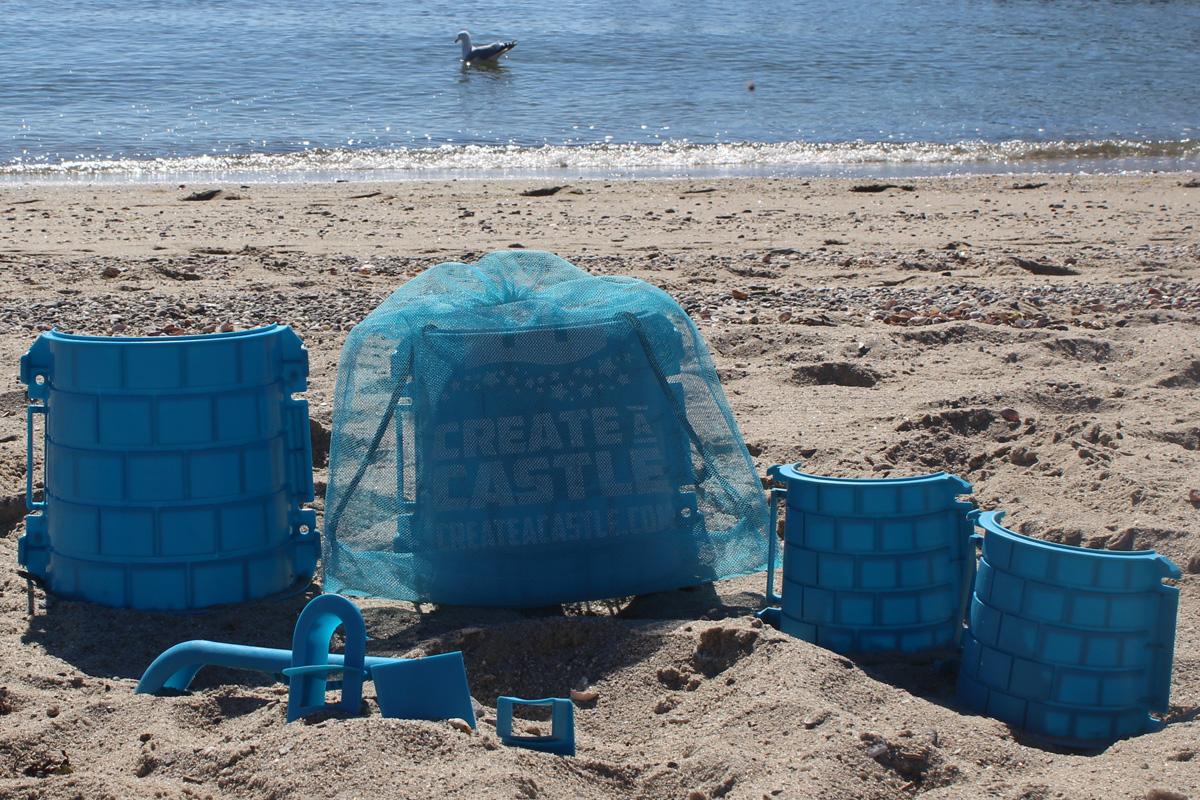 Blue mesh Create A Castle bag surrounded by tower mold pieces and blue detailing tools on the beach.