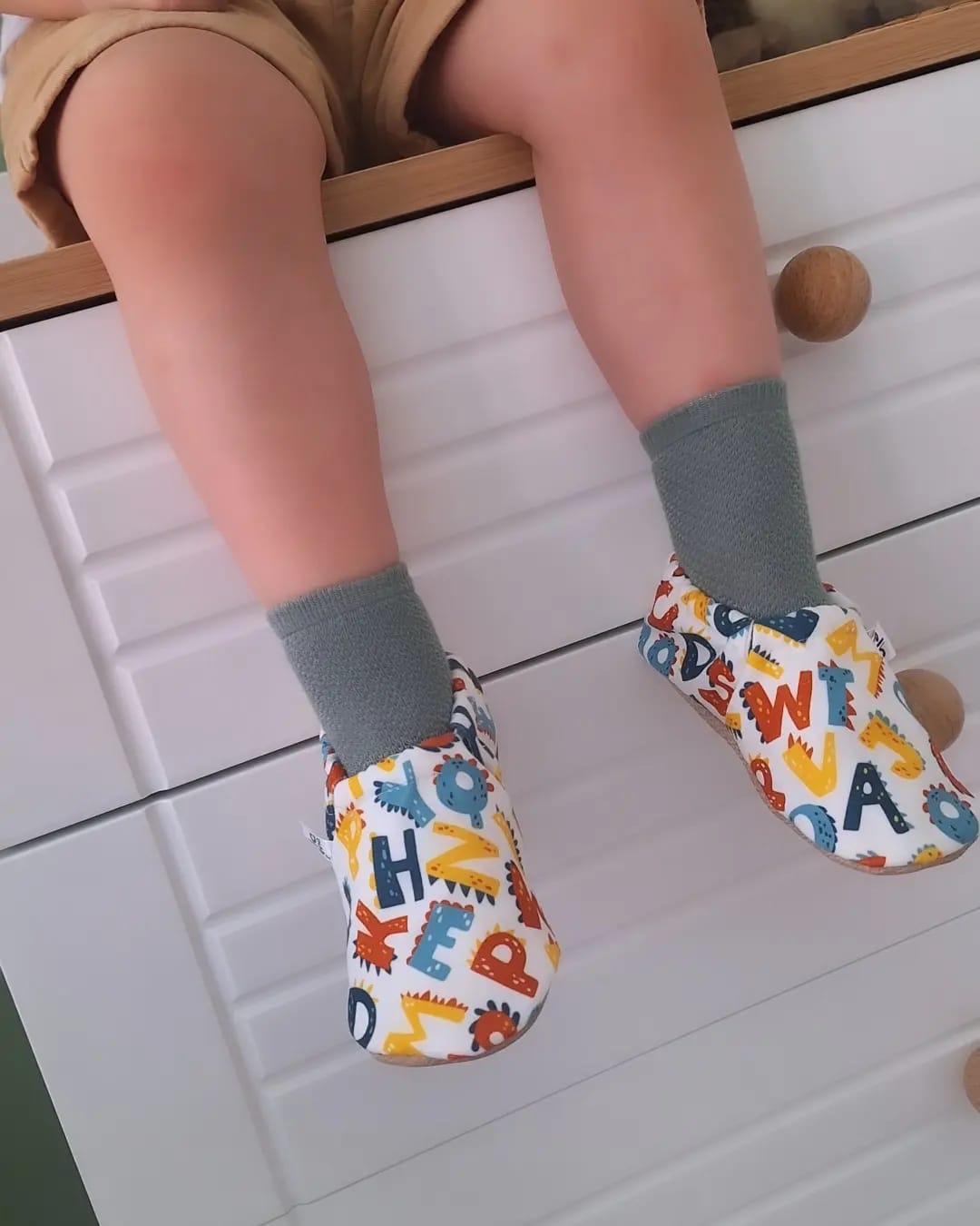 Close-up of alphabet-print moccasins worn with gray socks.