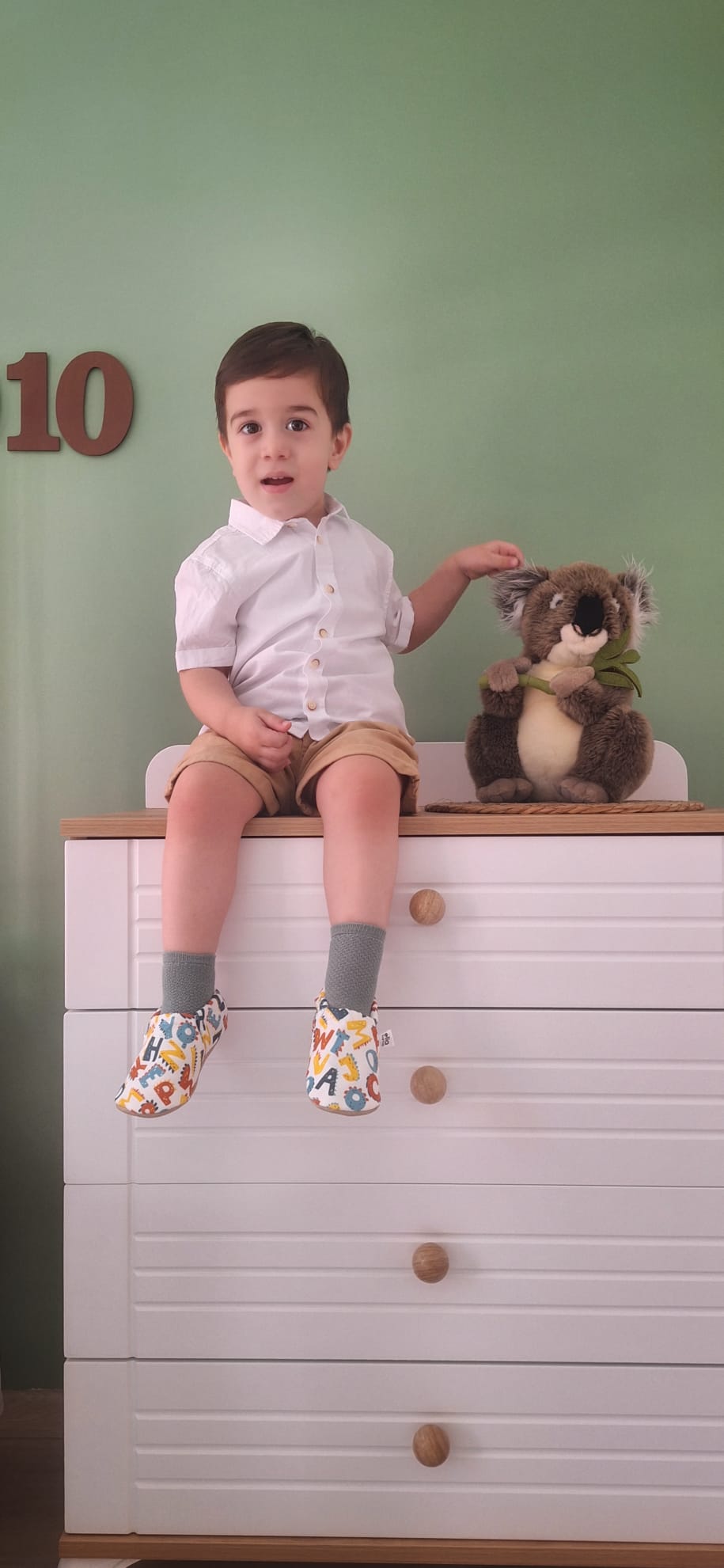 Child seated on a dresser wearing alphabet-print moccasins.