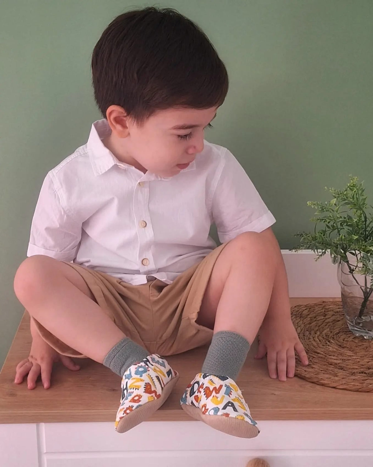 Child sitting cross-legged wearing alphabet-print moccasins.