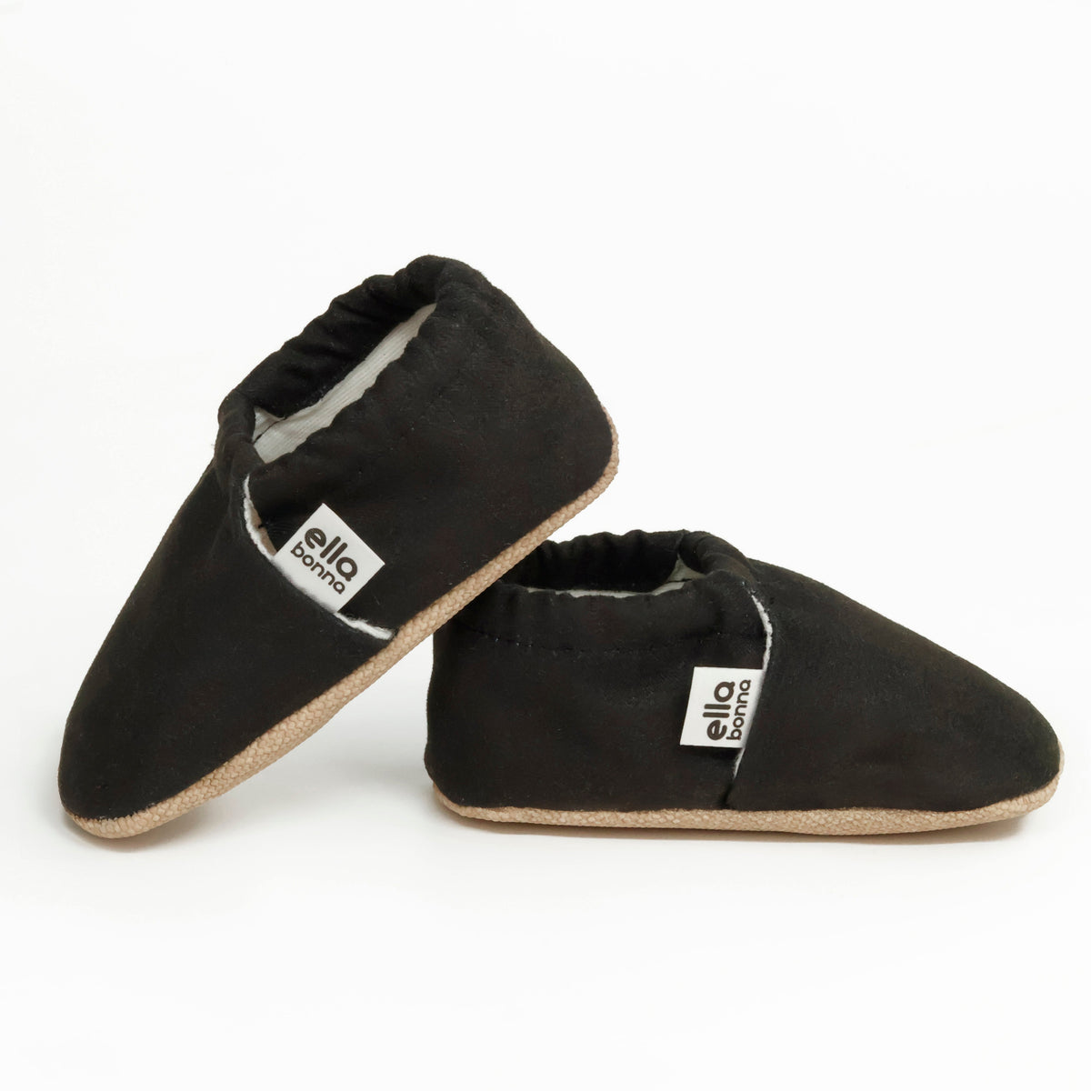Side views of black slip-on baby moccasins with cream lining and tan soles on a white background.
