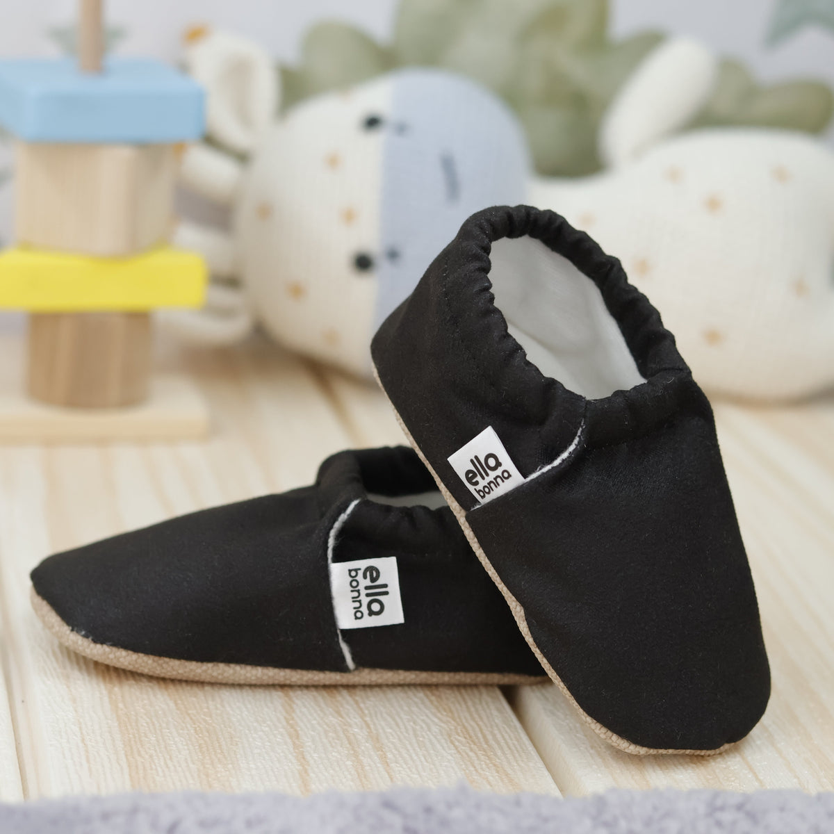 Black slip-on baby moccasins with cream lining and tan soles arranged together to show the sides and uppers.