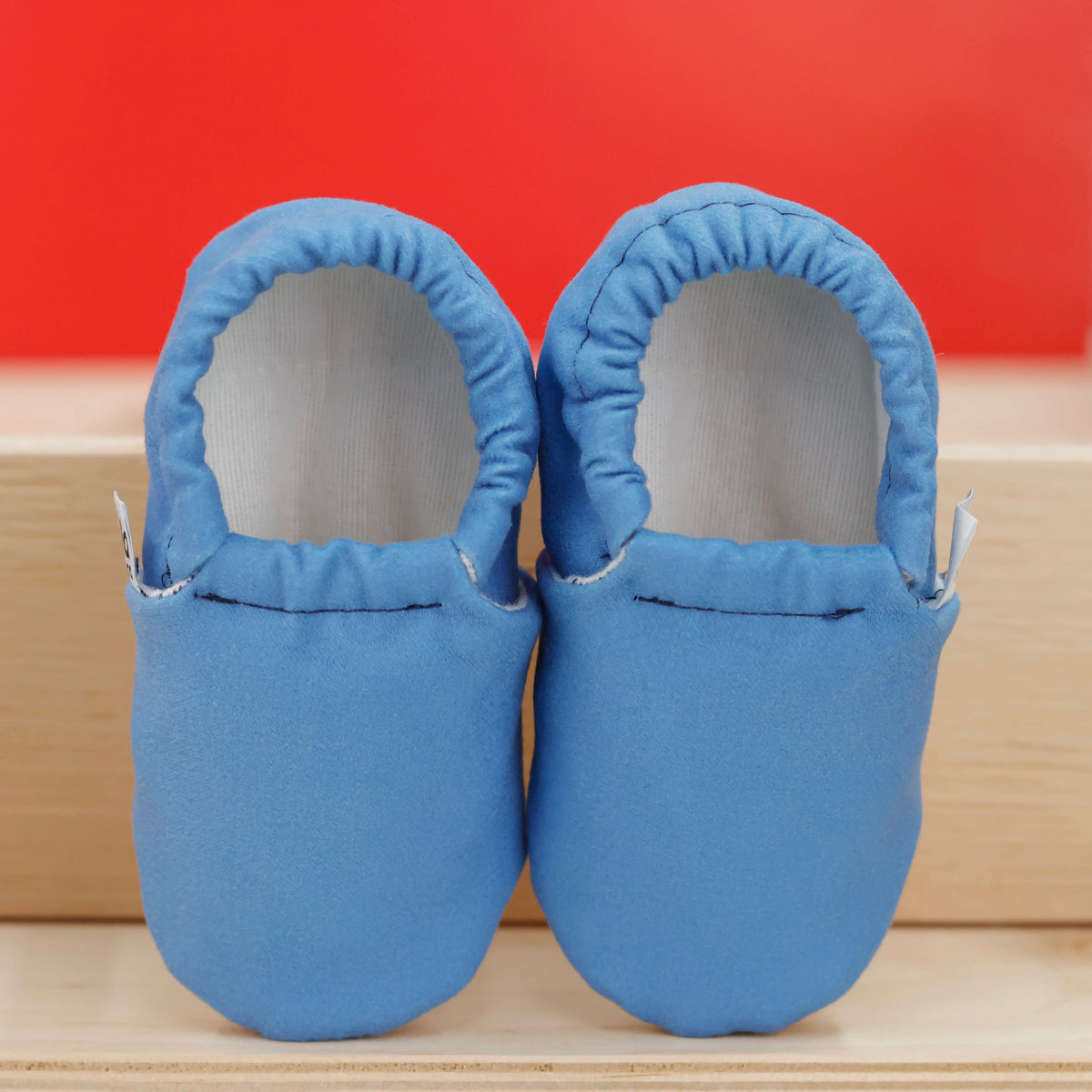 Front view of a pair of blue slip-on baby moccasins with cream lining and tan soles.