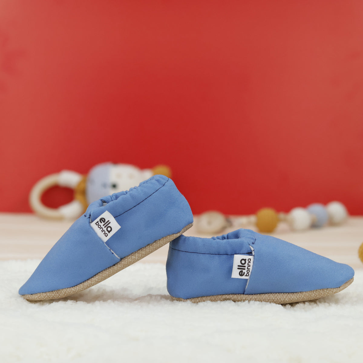 Blue slip-on baby moccasins with cream lining and tan soles arranged together to show the sides and uppers.
