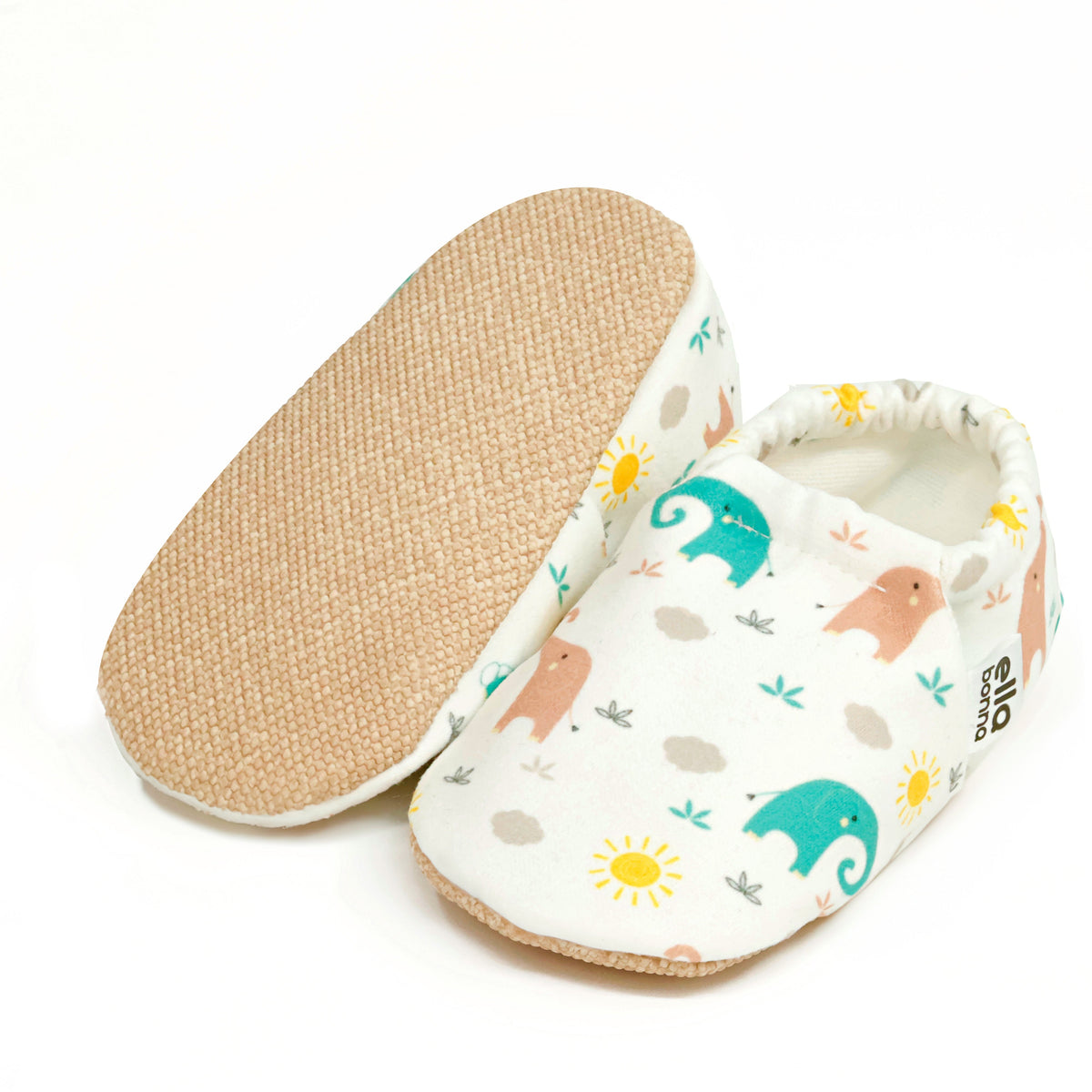 Cream slip-on baby moccasins with pastel elephant print, with one sole facing the camera on a white background.