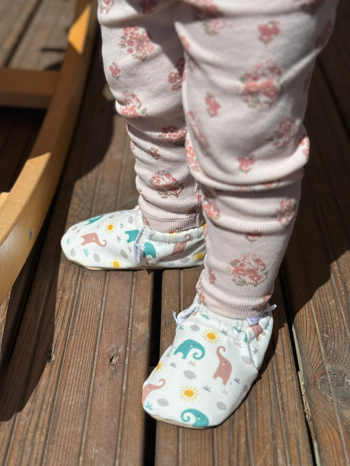 Close-up of elephant-print moccasins worn on a wooden deck.