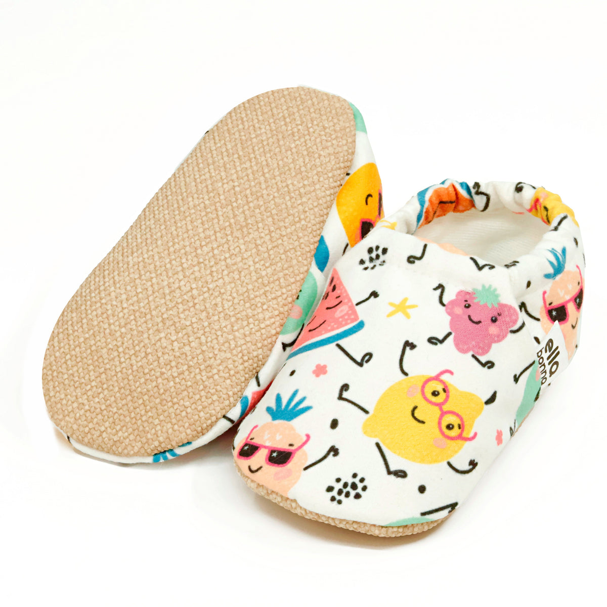 Cream slip-on baby moccasins with colorful smiling fruit print, with one sole facing the camera on a white background.