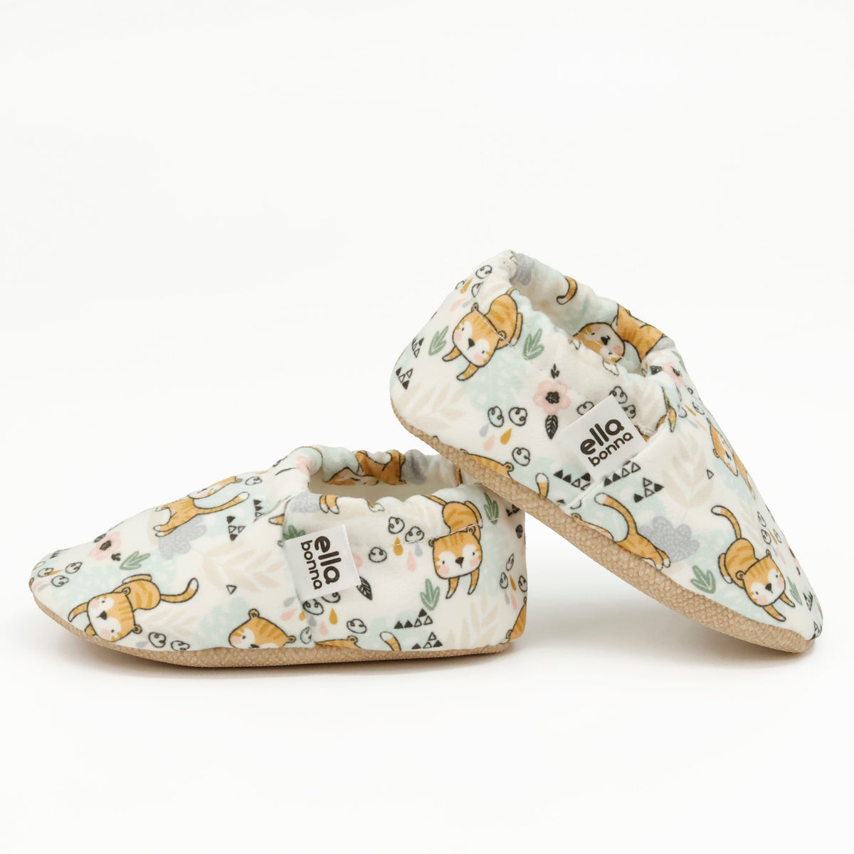 Side views of cream slip-on baby moccasins with small yellow cat print on a white background.