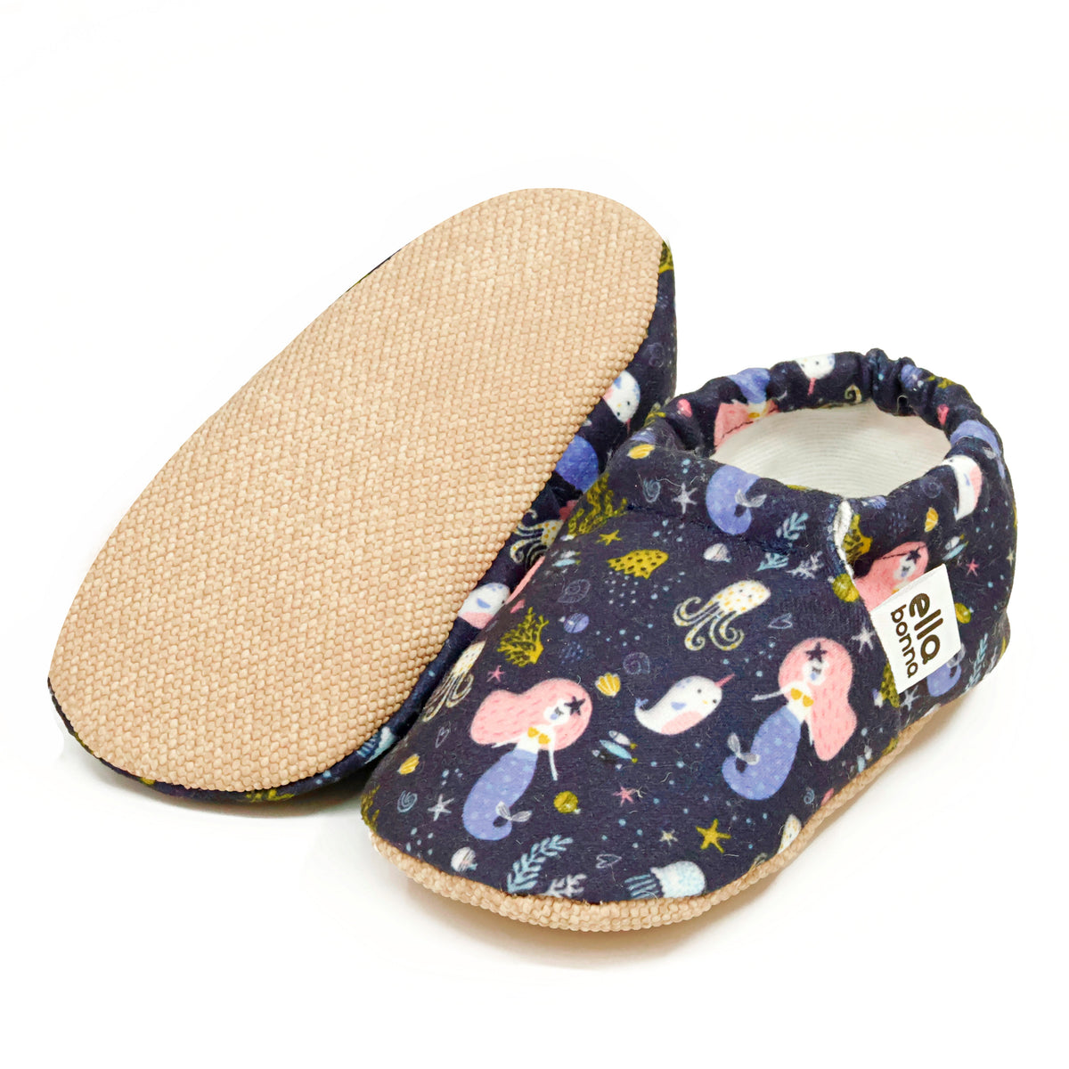 Navy slip-on baby moccasins with mermaids and sea-creature print, with one sole facing the camera on a white background.