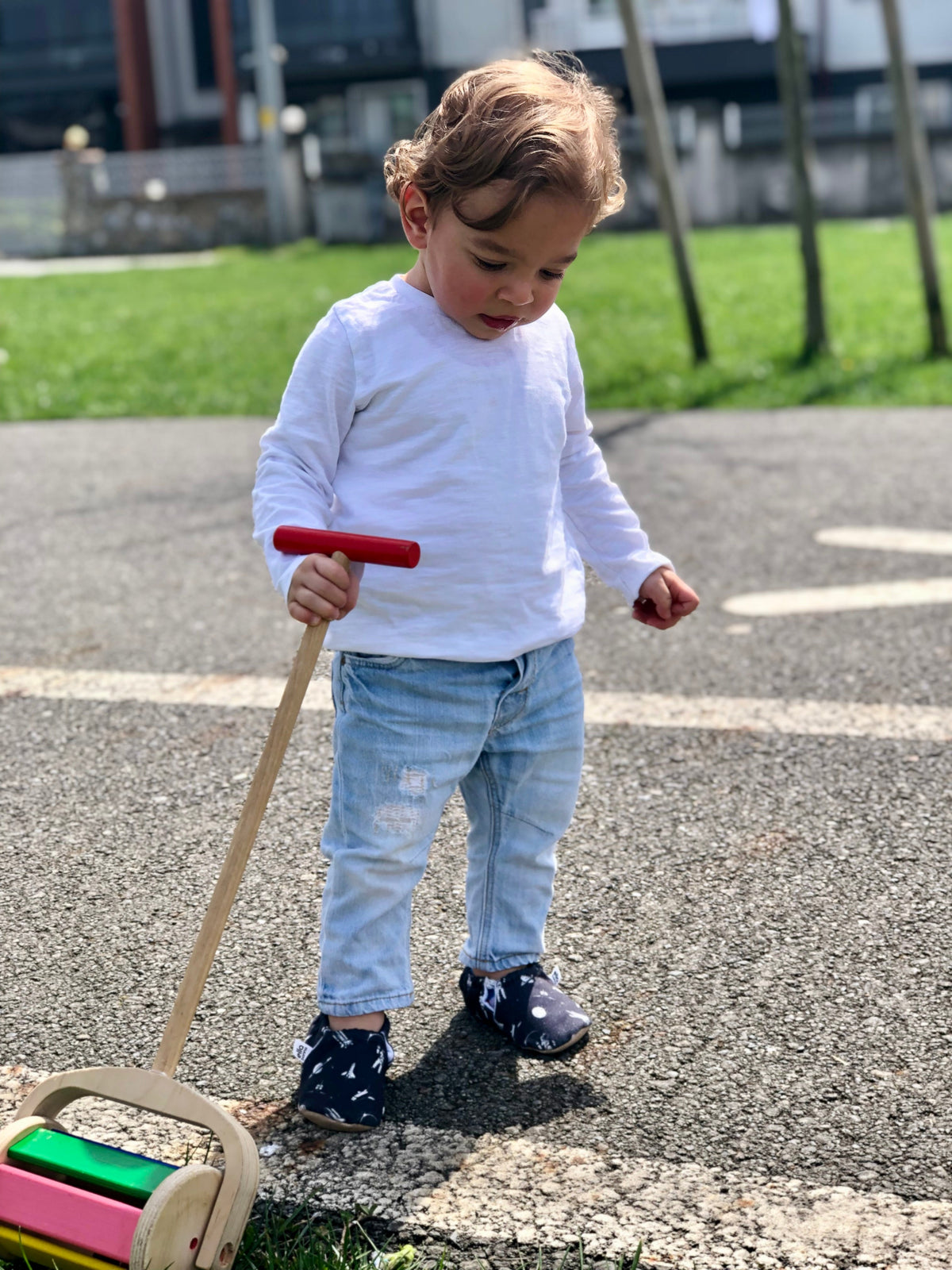 Child standing outdoors with a push toy wearing dark moccasins.