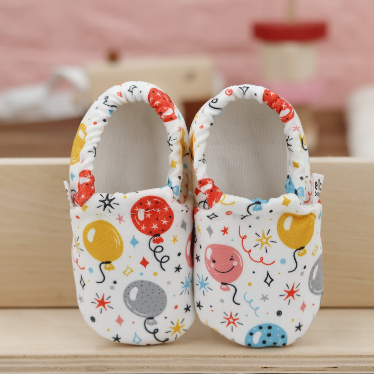 Pair of cream slip-on baby moccasins with colorful balloon print, showing the openings and uppers.