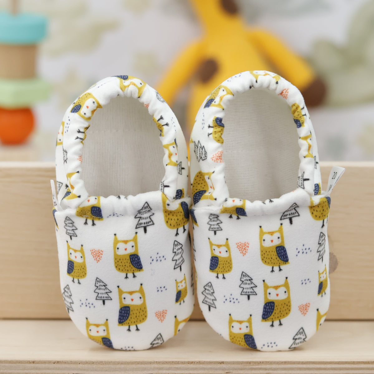Pair of cream slip-on baby moccasins with yellow owl and tree print, showing the openings and uppers.