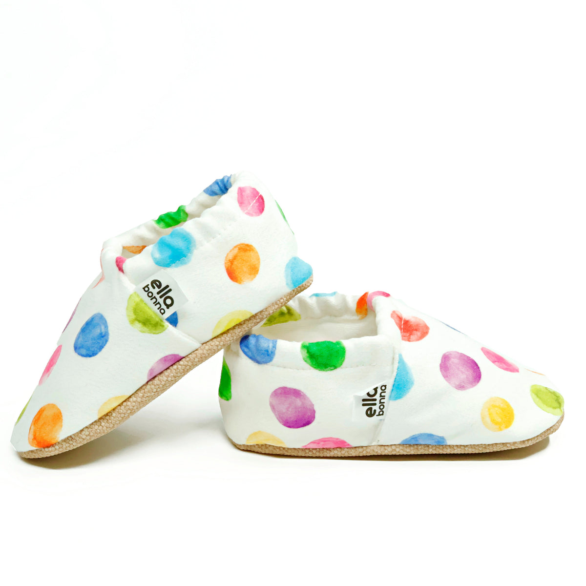 Side views of white slip-on baby moccasins with multicolored watercolor dot print on a white background.