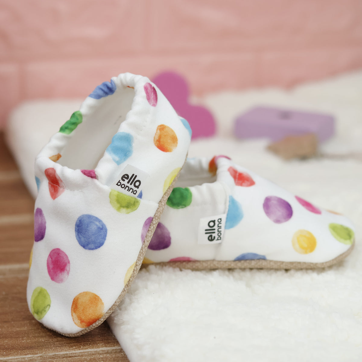 White slip-on baby moccasins with multicolored watercolor dot print arranged together to show the sides and uppers.