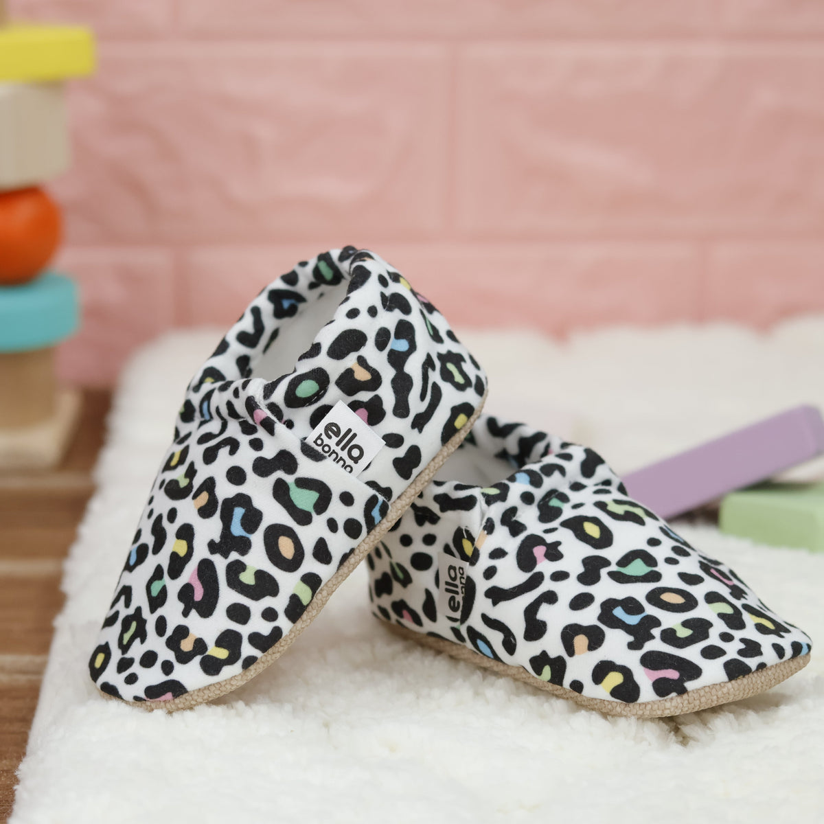 Cream slip-on baby moccasins with multicolored leopard spots arranged together to show the sides and uppers.