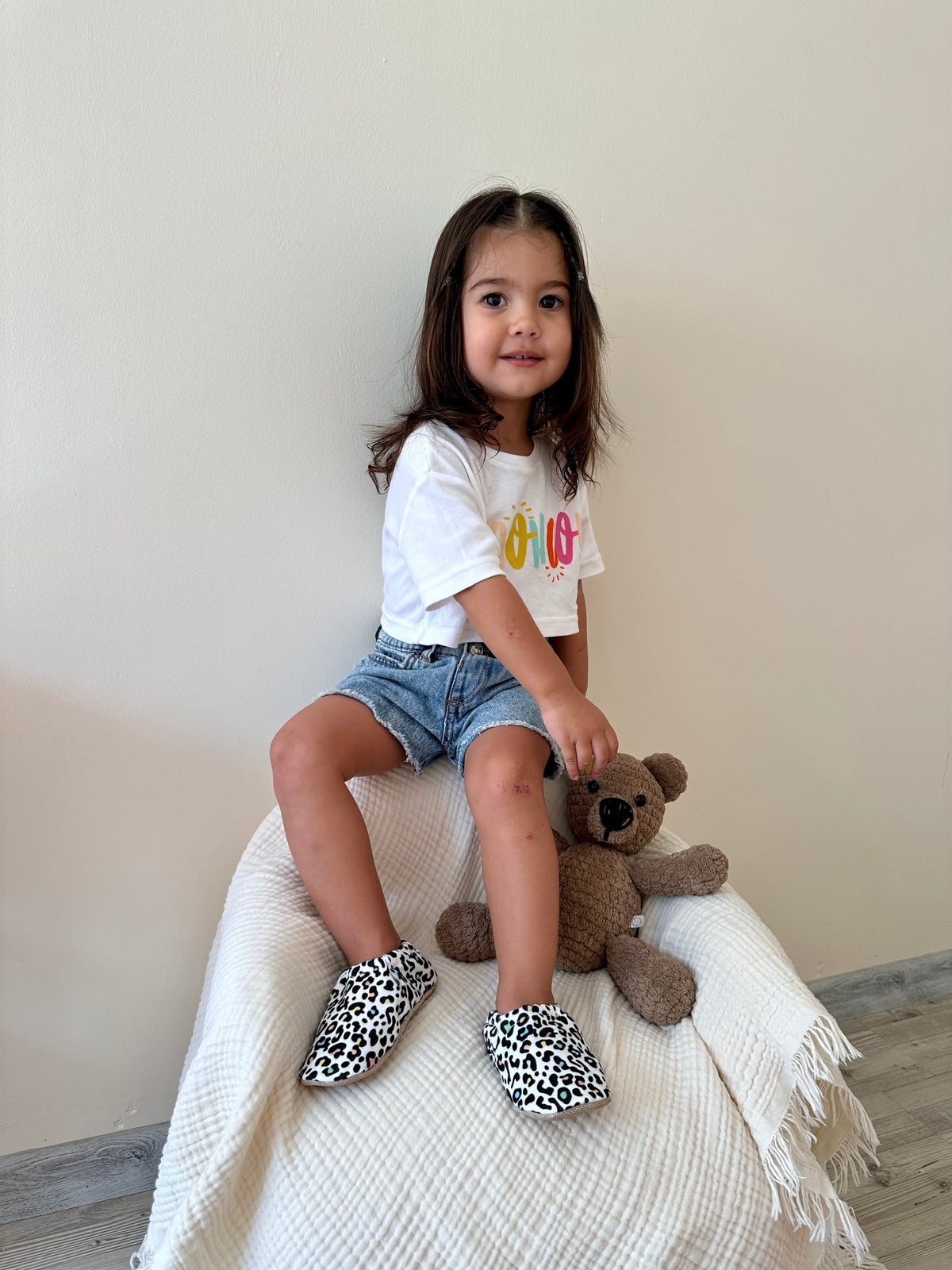 Child seated on a stool wearing leopard-print moccasins.