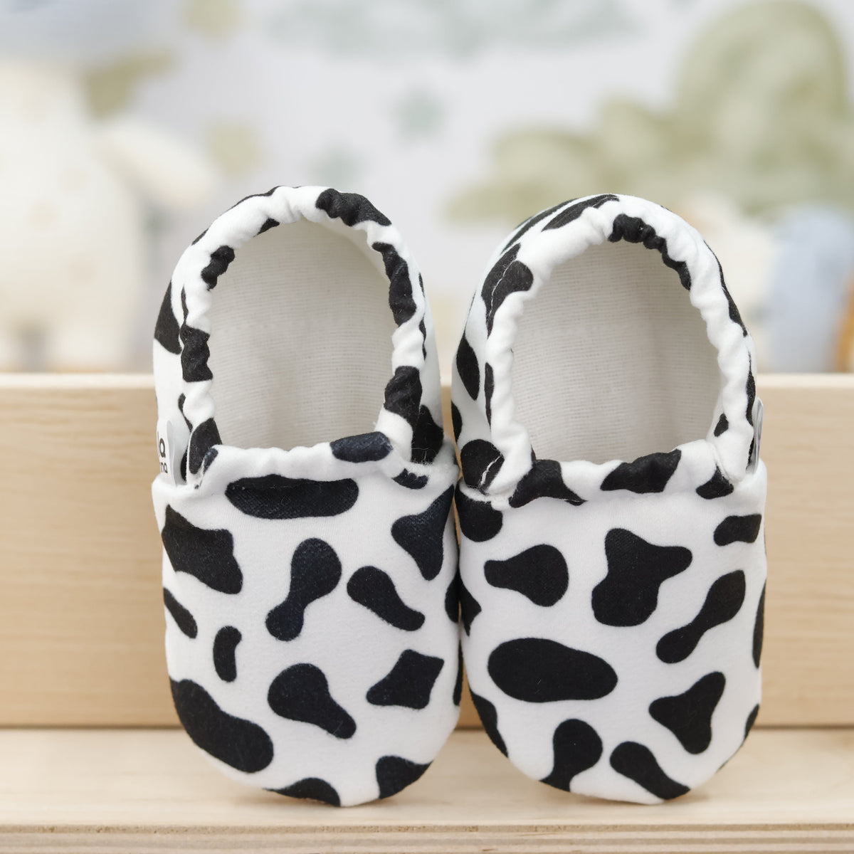 Pair of white slip-on baby moccasins with black cow spots, showing the openings and uppers.