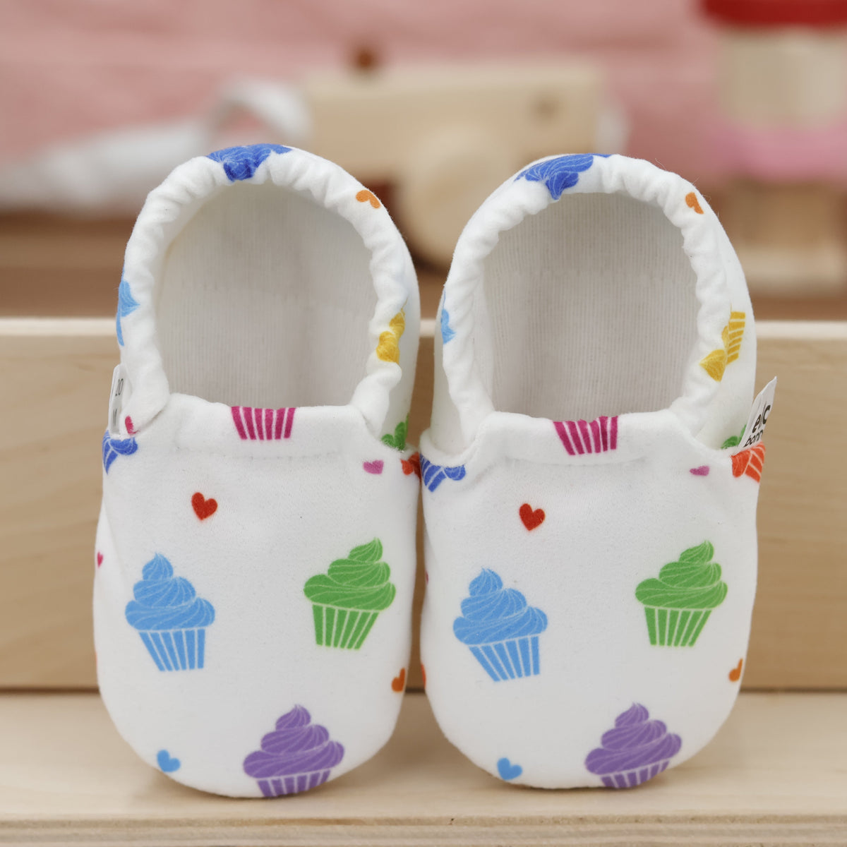 Pair of white slip-on baby moccasins with colorful cupcake print, showing the openings and uppers.
