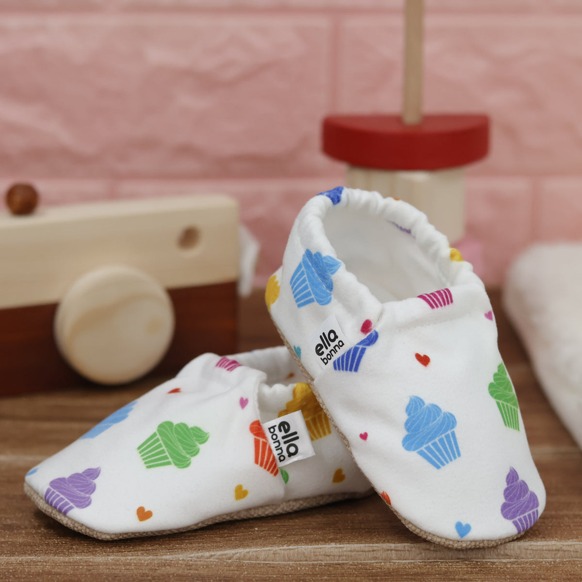 White slip-on baby moccasins with colorful cupcake print arranged together to show the sides and uppers.